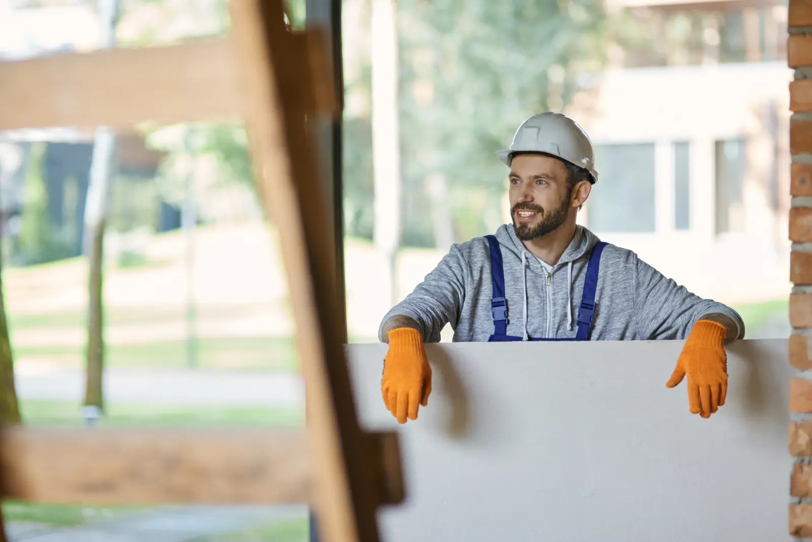 Mastering Plasterboard Finishing. young male builder in hard hat looking positive, holding drywall.